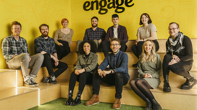 New recruits at Engage - a team of 10 sits in front of a yellow wall